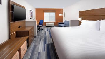 A hotel room with a bed, a desk with a flat-screen TV, a chair, a sofa, and a window with a view.