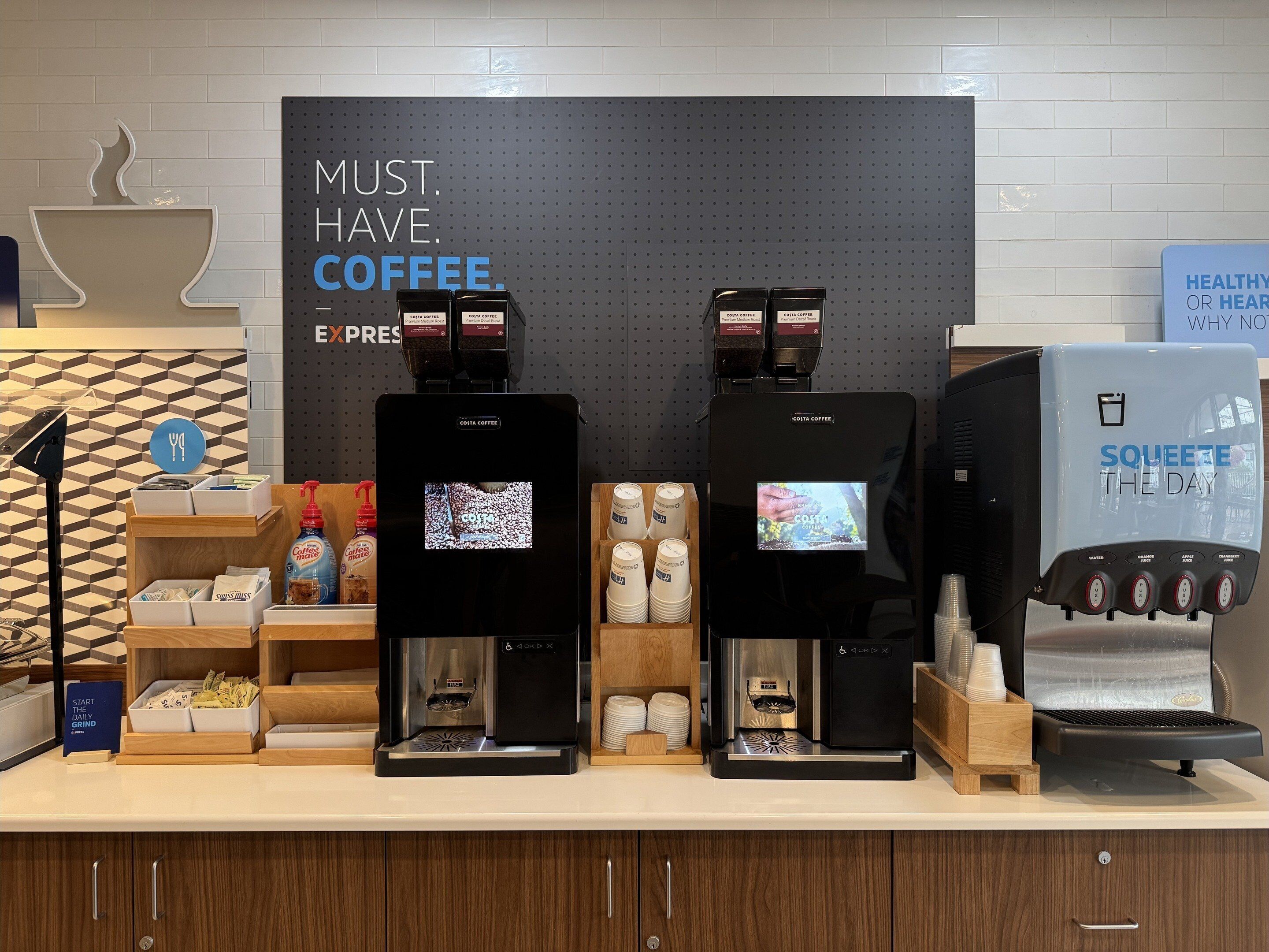 A coffee station with two espresso machines, a water dispenser, and a sign that reads "MUST HAVE COFFEE".