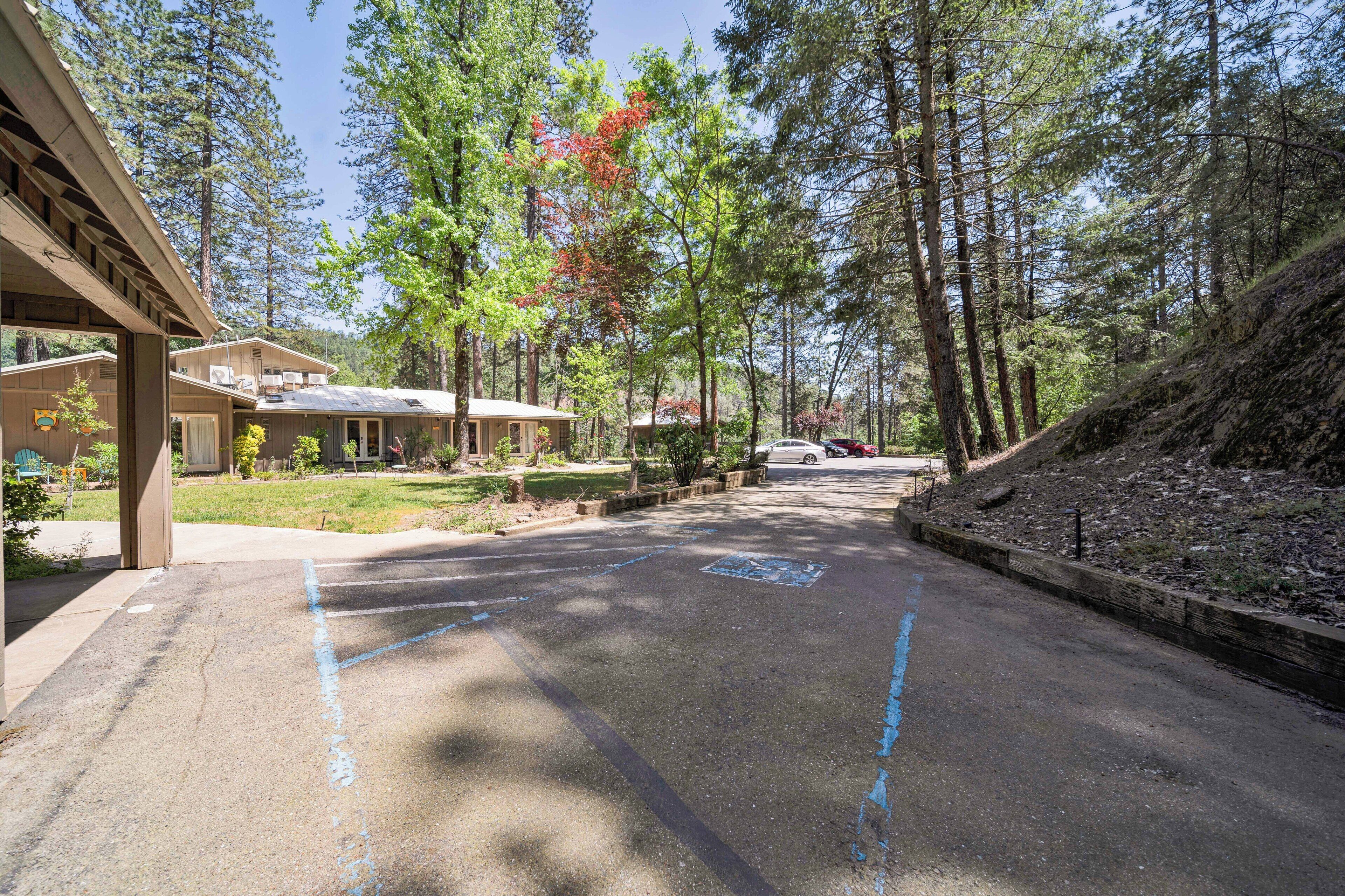 A parking lot with marked spaces, a building with a covered entrance, and a forested hillside.
