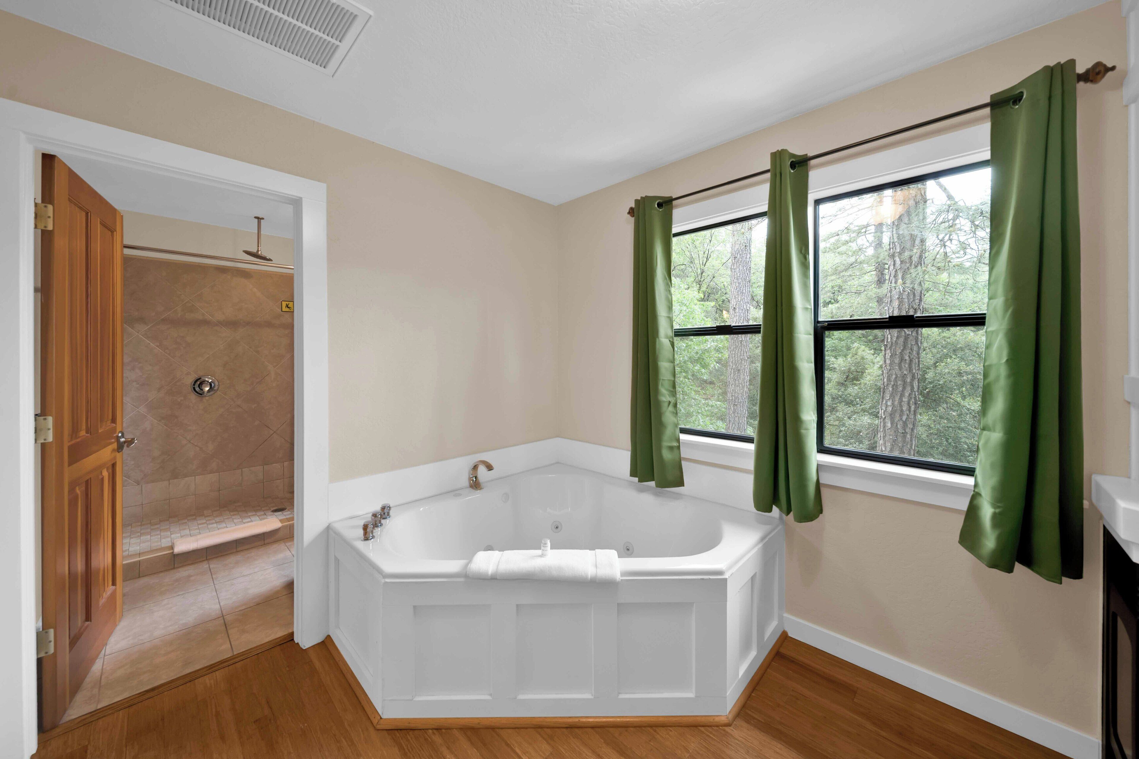 A bathroom with a freestanding bathtub, a shower, and a window with curtains.