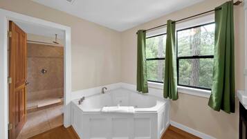 A bathroom with a freestanding bathtub, a shower, and a window with curtains.
