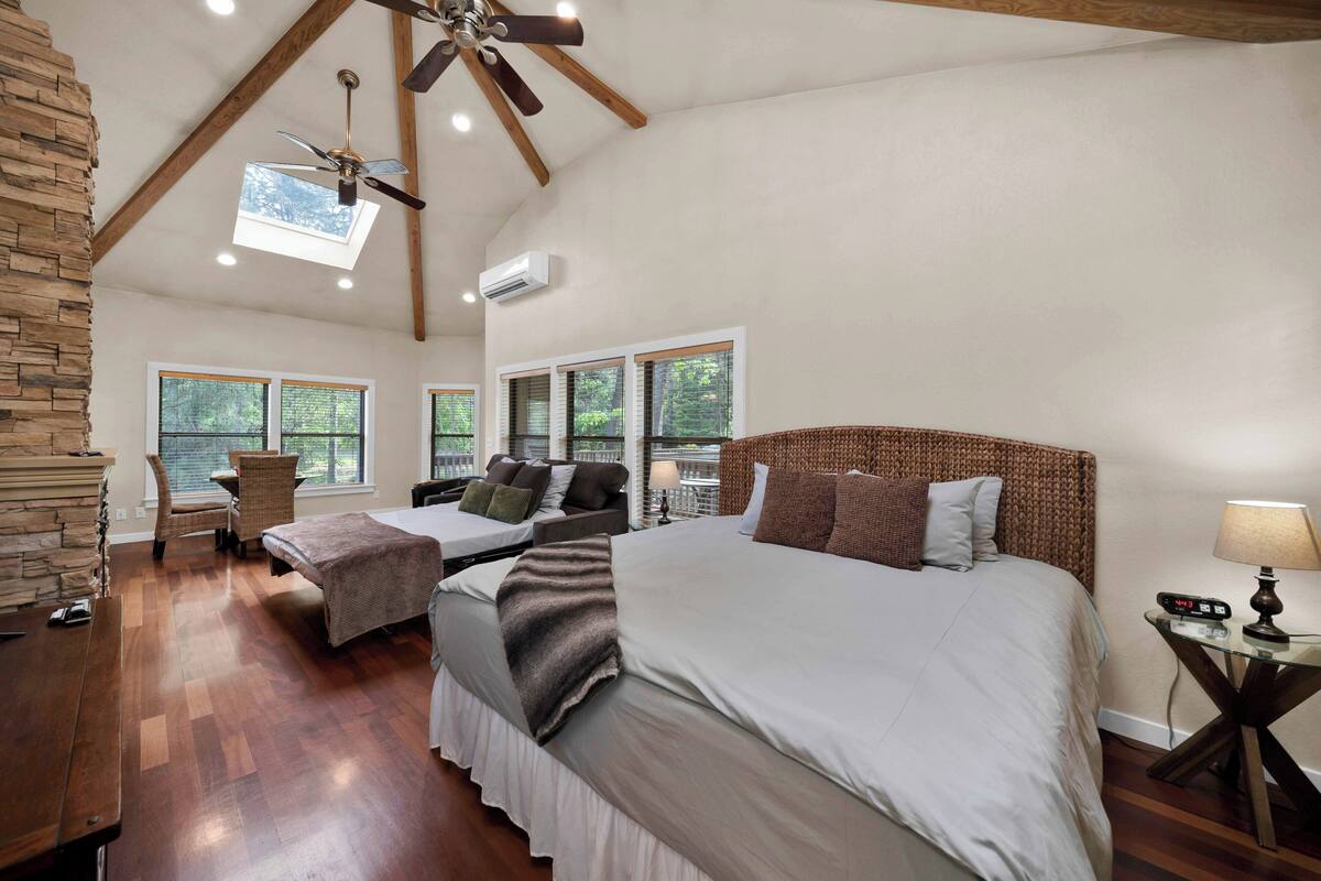A spacious bedroom with a large bed, two smaller beds, a stone accent wall, and a skylight.