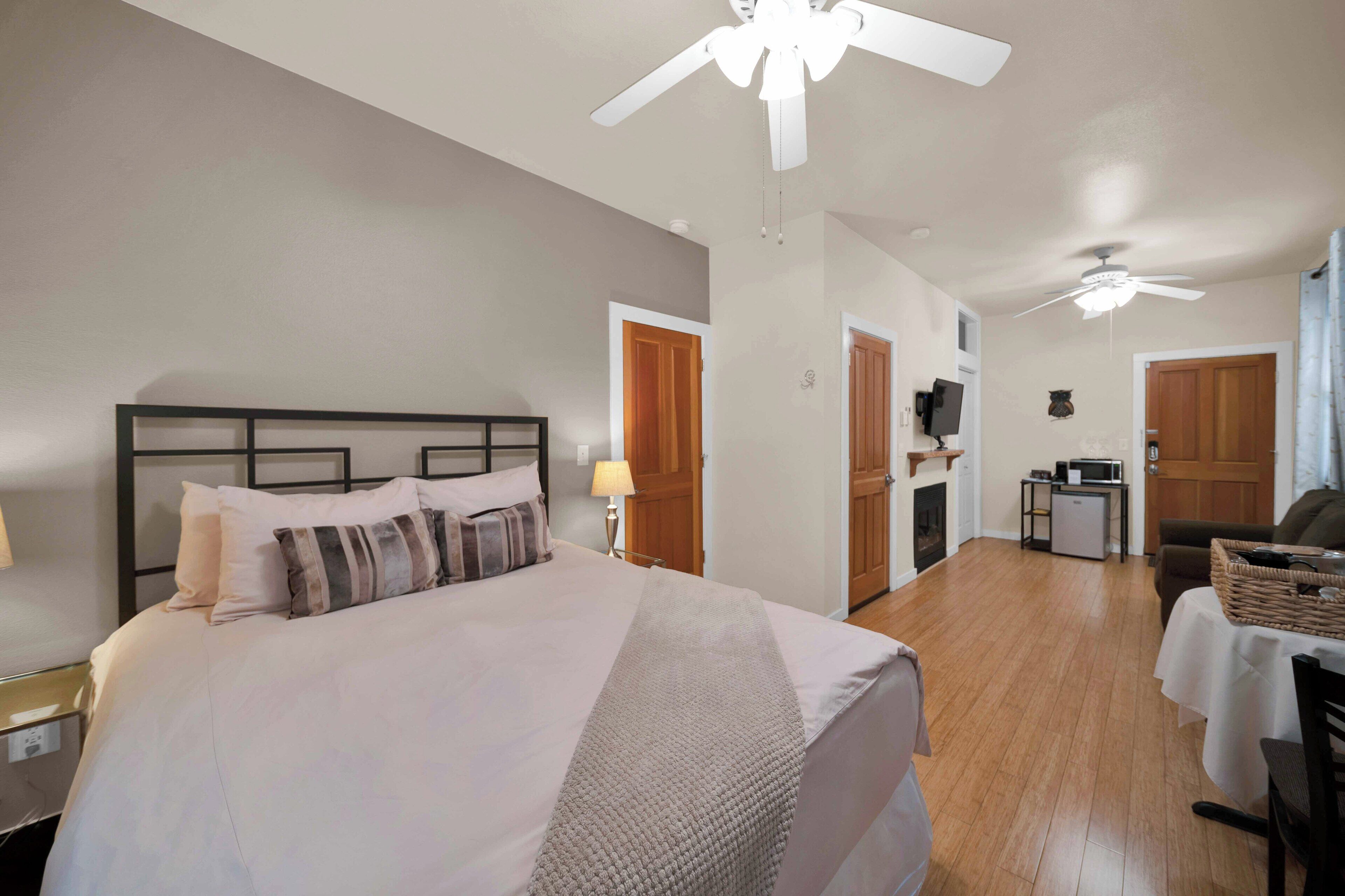 A hotel room with a bed, a ceiling fan, a kitchenette, and a dining area.