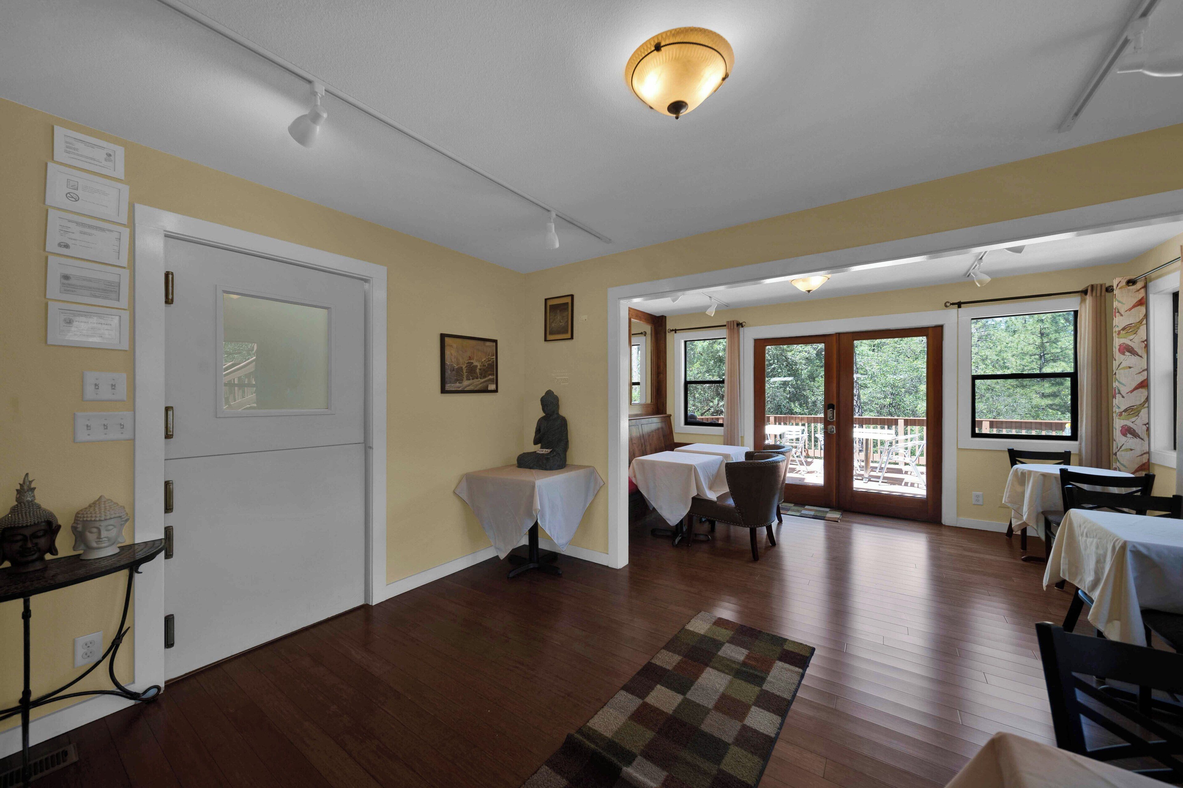 A spacious room with wooden flooring, a dining area with tables and chairs, and a statue on a pedestal.