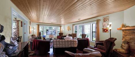 A spacious room with wooden ceiling, multiple seating areas, a fireplace, and large windows providing natural light.