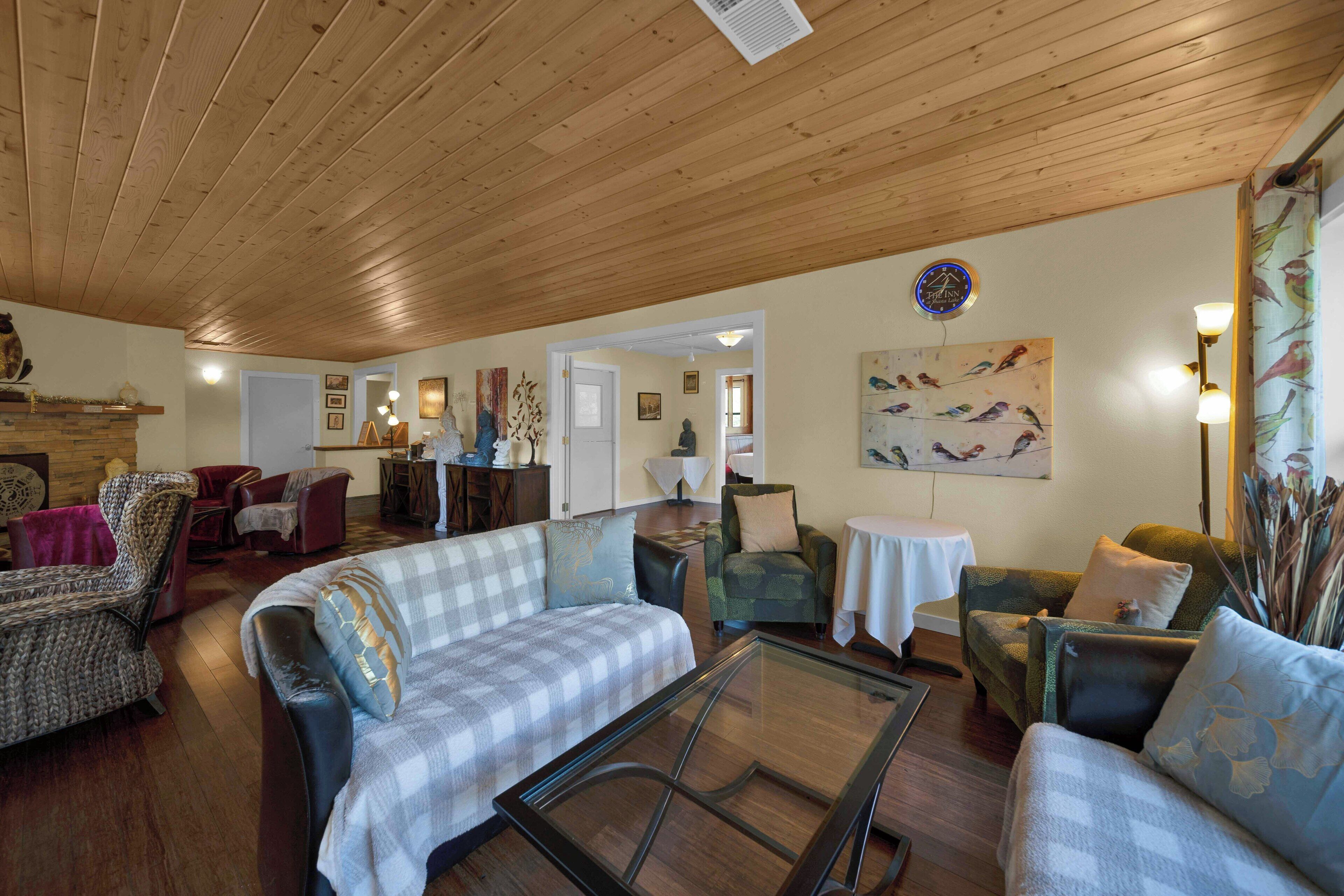 A spacious living room with wooden ceilings, a glass coffee table, and various seating options including a sofa and armchairs.