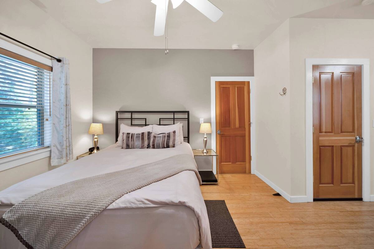 A bedroom with a bed, bedside lamps, a wooden door, and a window with blinds.