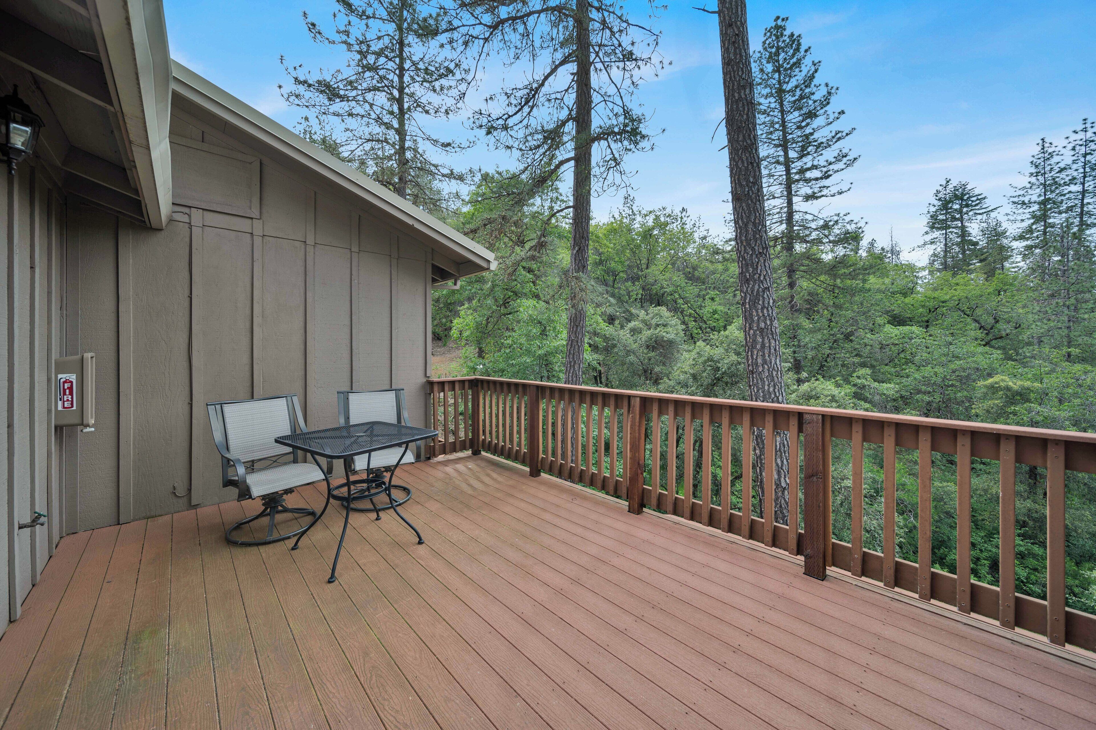 Une terrasse en bois avec une table et des chaises, donnant sur une zone boisée.