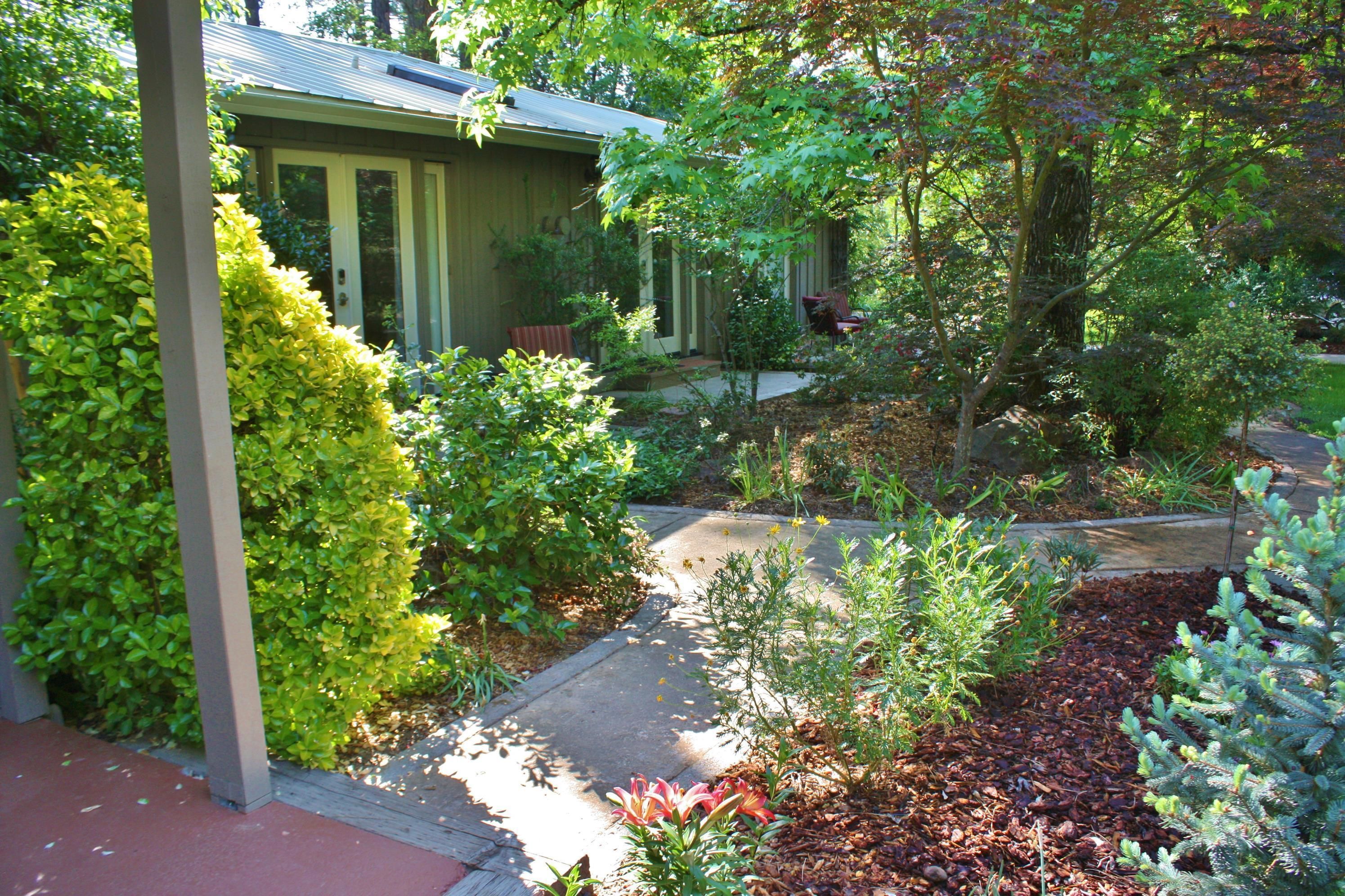 A residential garden with a pathway leading to a house with a porch.