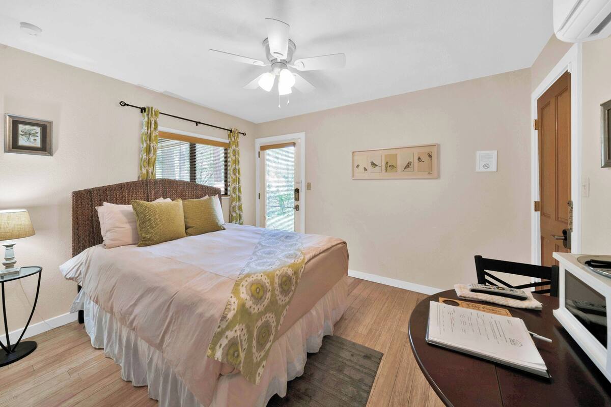 A bedroom with a bed, a ceiling fan, a desk with a chair, a lamp, and a window with curtains.