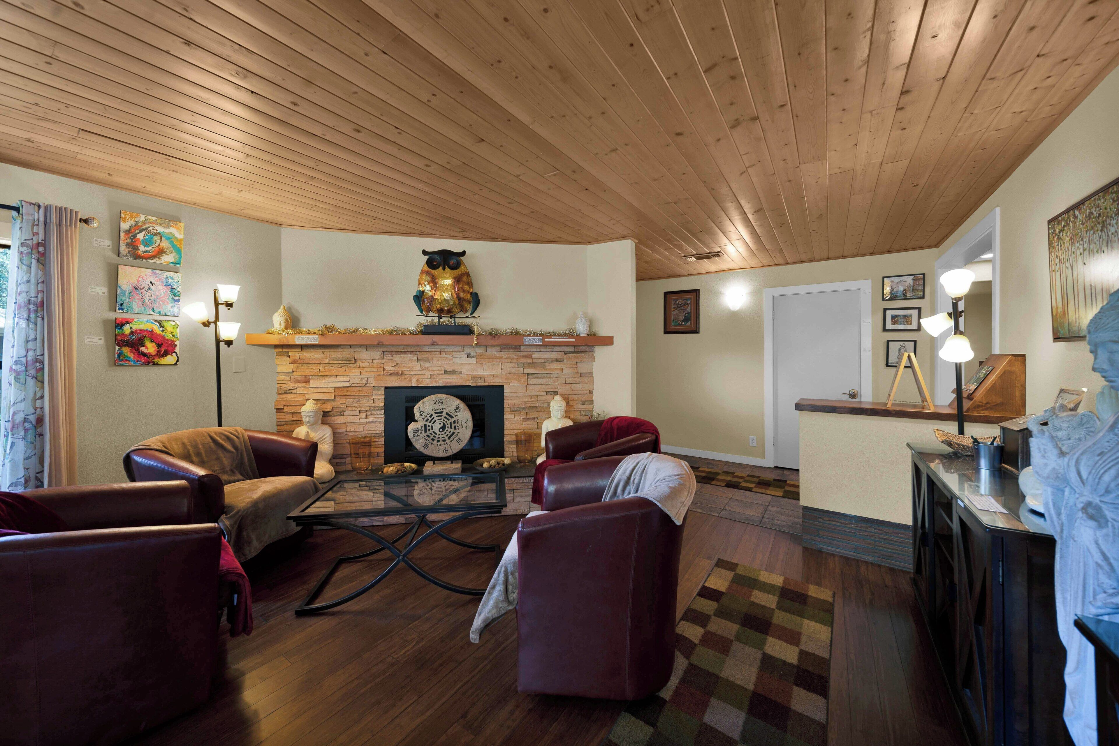 A cozy living room with a fireplace, leather chairs, and a wooden ceiling.