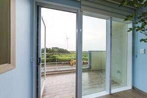 Een kamer met een schuifdeur die uitkomt op een buitenruimte, met uitzicht op een windturbine en bouwmachines.