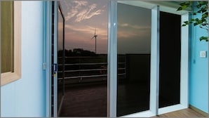 Une pièce dotée d’une porte-fenêtre coulissante donnant sur un balcon d’où l’on peut admirer une éolienne et un ciel au coucher du soleil.