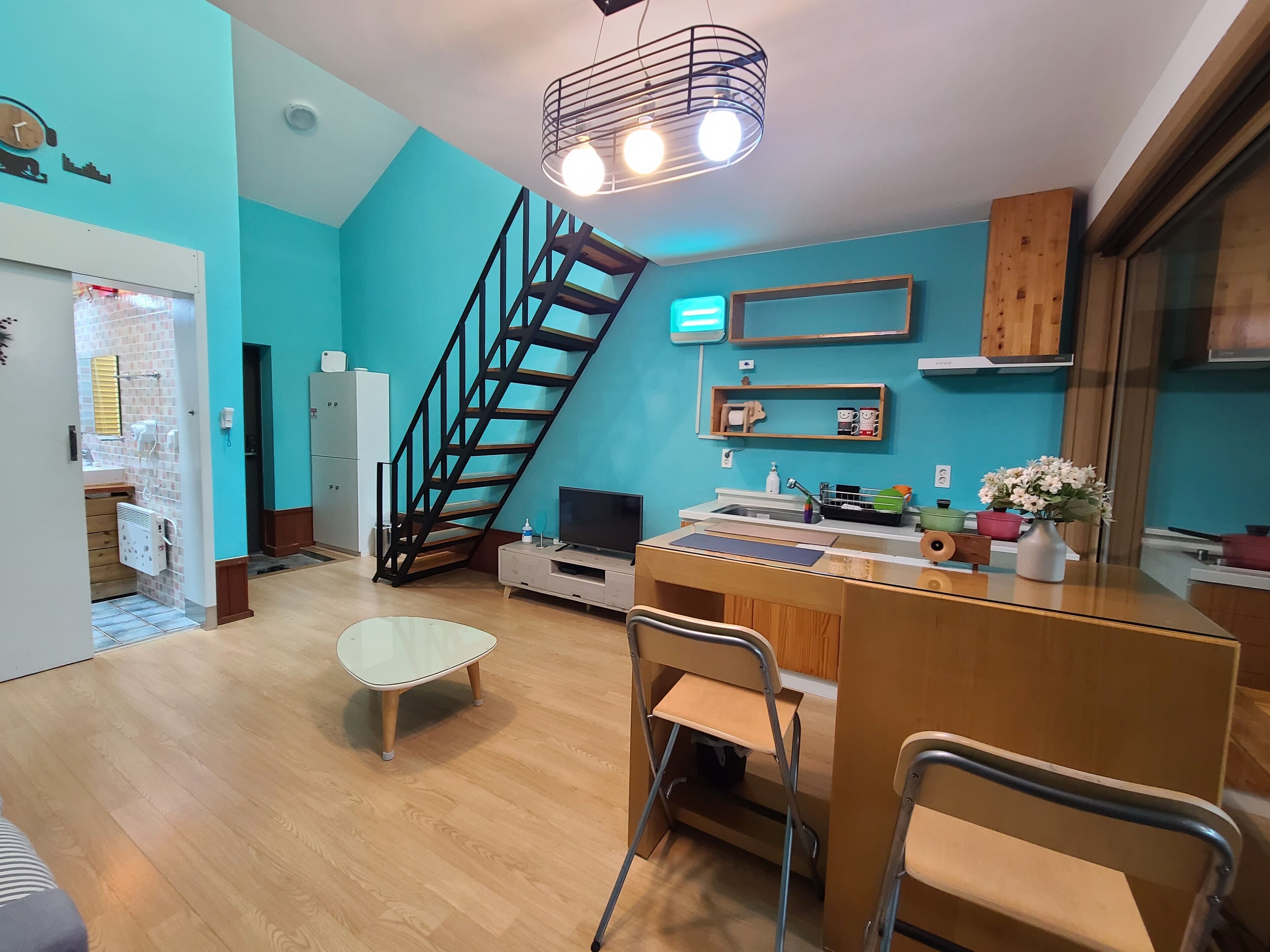 A modern kitchen with a wooden staircase, a dining area with a white table and chairs, and a kitchen island with a sink and countertop.