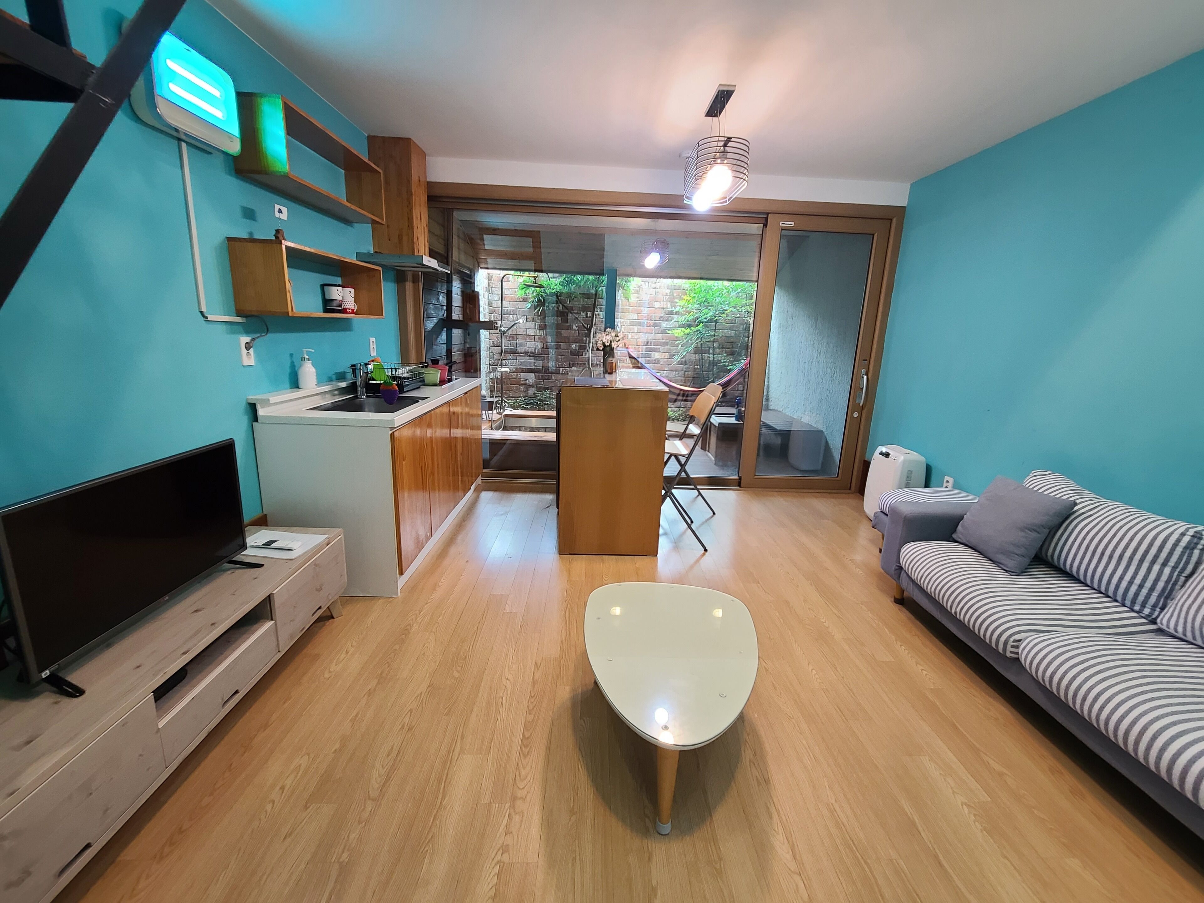 A modern living room with a flat-screen TV, a sofa, a coffee table, and a kitchen area with a sink and cabinets.