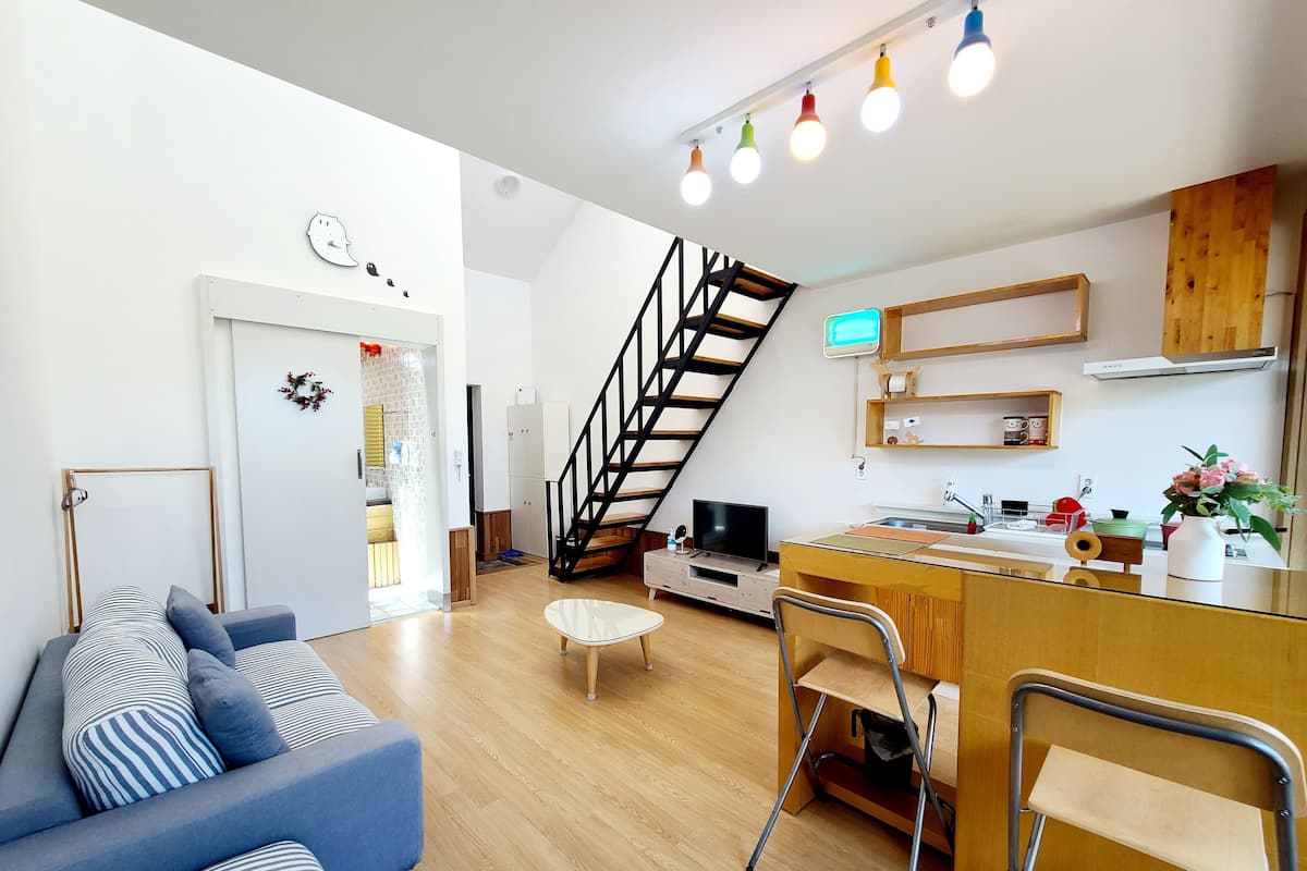 A modern living space with a sofa, a dining area, a kitchen, and a staircase.