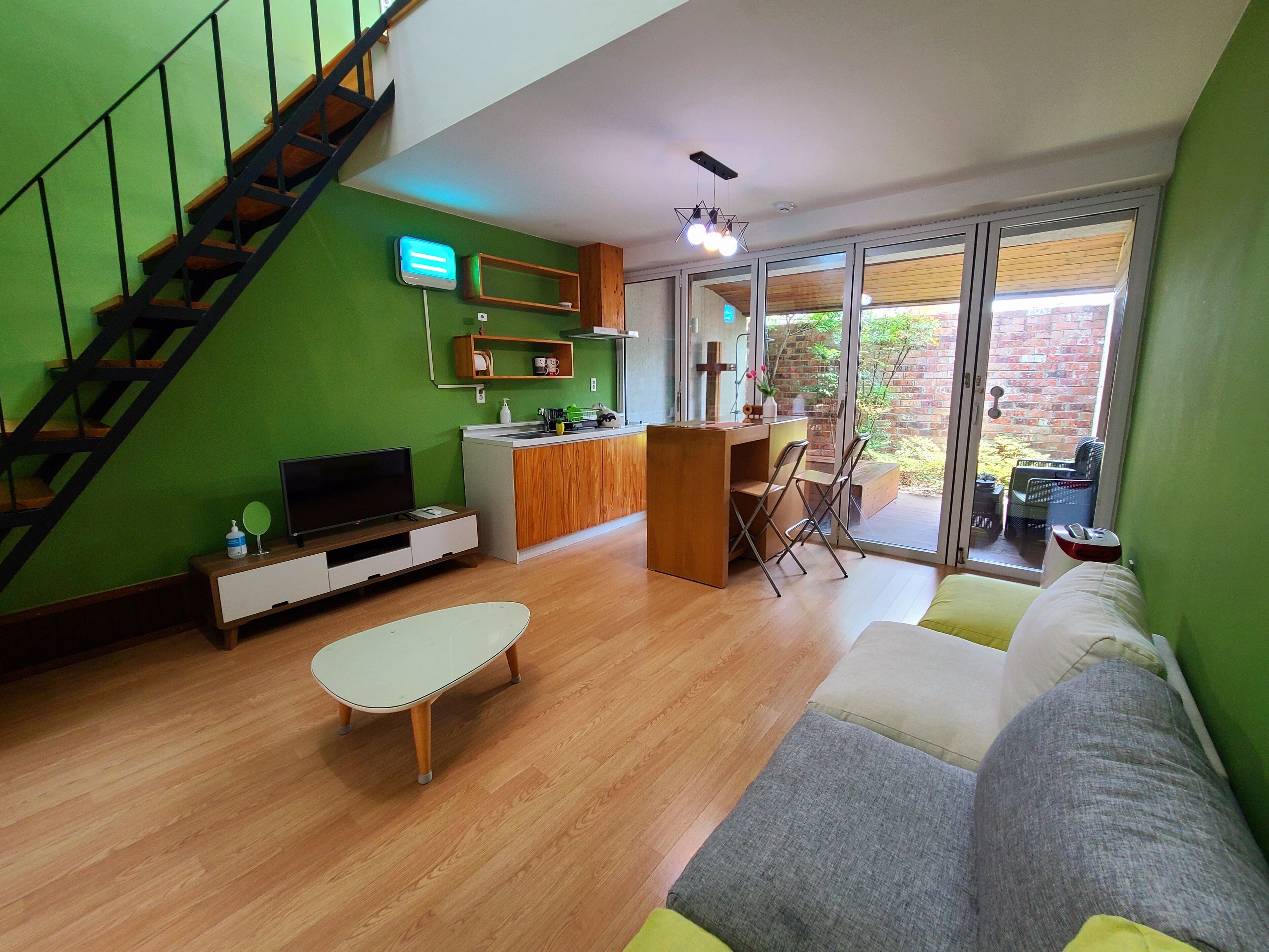 Een moderne woonkamer met een trap, een flatscreen televisie, een eethoek en een grote schuifpui die leidt naar een terras.