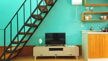 A room with teal walls, a wooden staircase, a TV on a cabinet, and a shelf with decorative items.