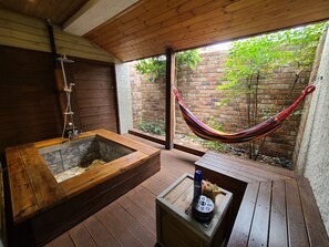A wooden deck with a hammock, a wooden bathtub, and a small table with a bottle and flowers. - Positano in Jeju (Seogwipo)