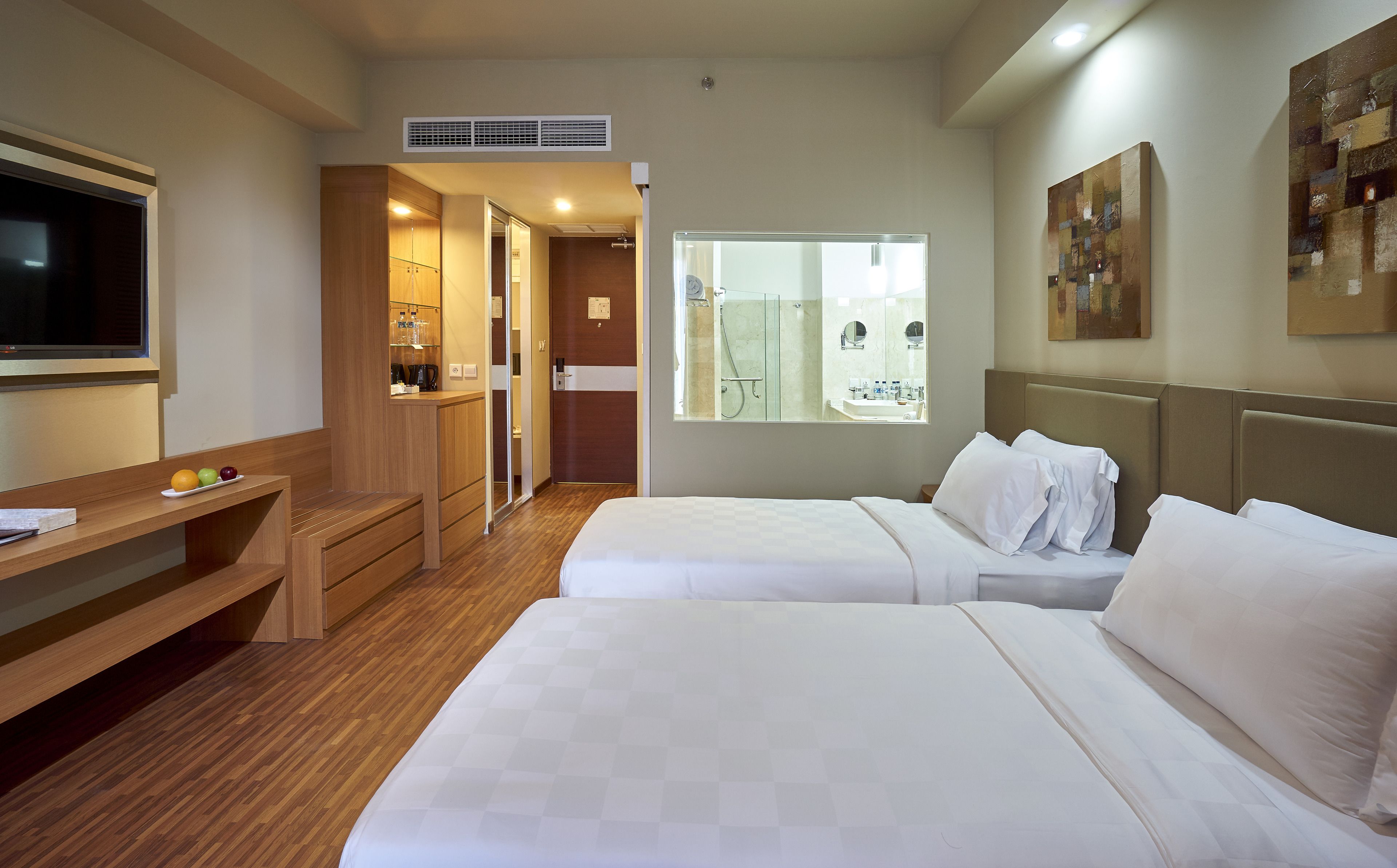 A hotel room with two beds, a TV, a desk with fruit, a shower, and a painting.