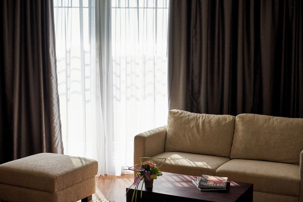 A living room with a beige sofa, a matching ottoman, and a coffee table with a magazine.