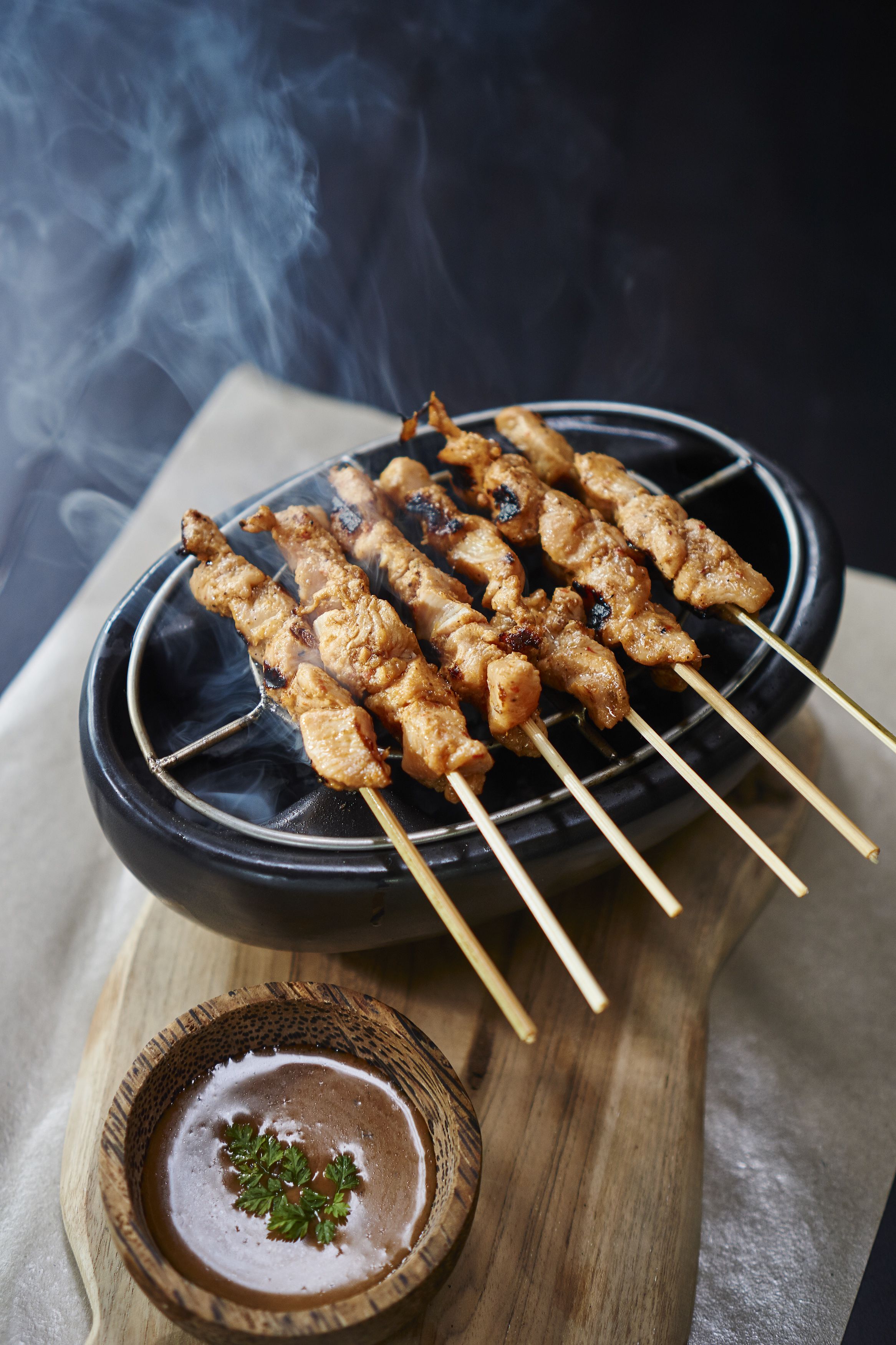 Skewers of grilled meat on a black plate with a small bowl of sauce.
