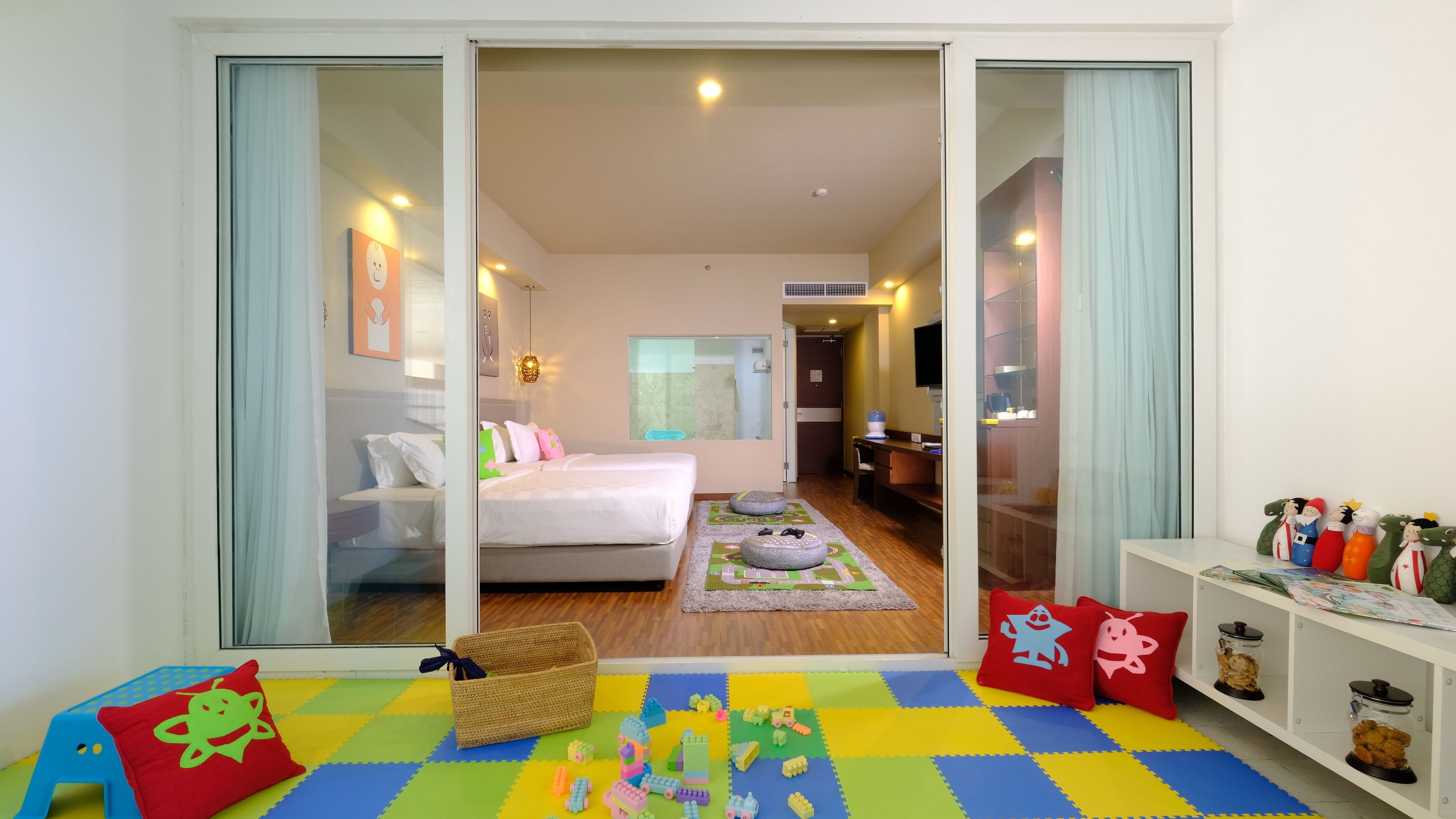 A hotel room with a bed, a small seating area with toys, and a play mat.