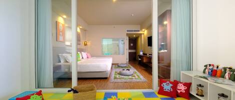 A hotel room with a bed, a small seating area with toys, and a play mat.