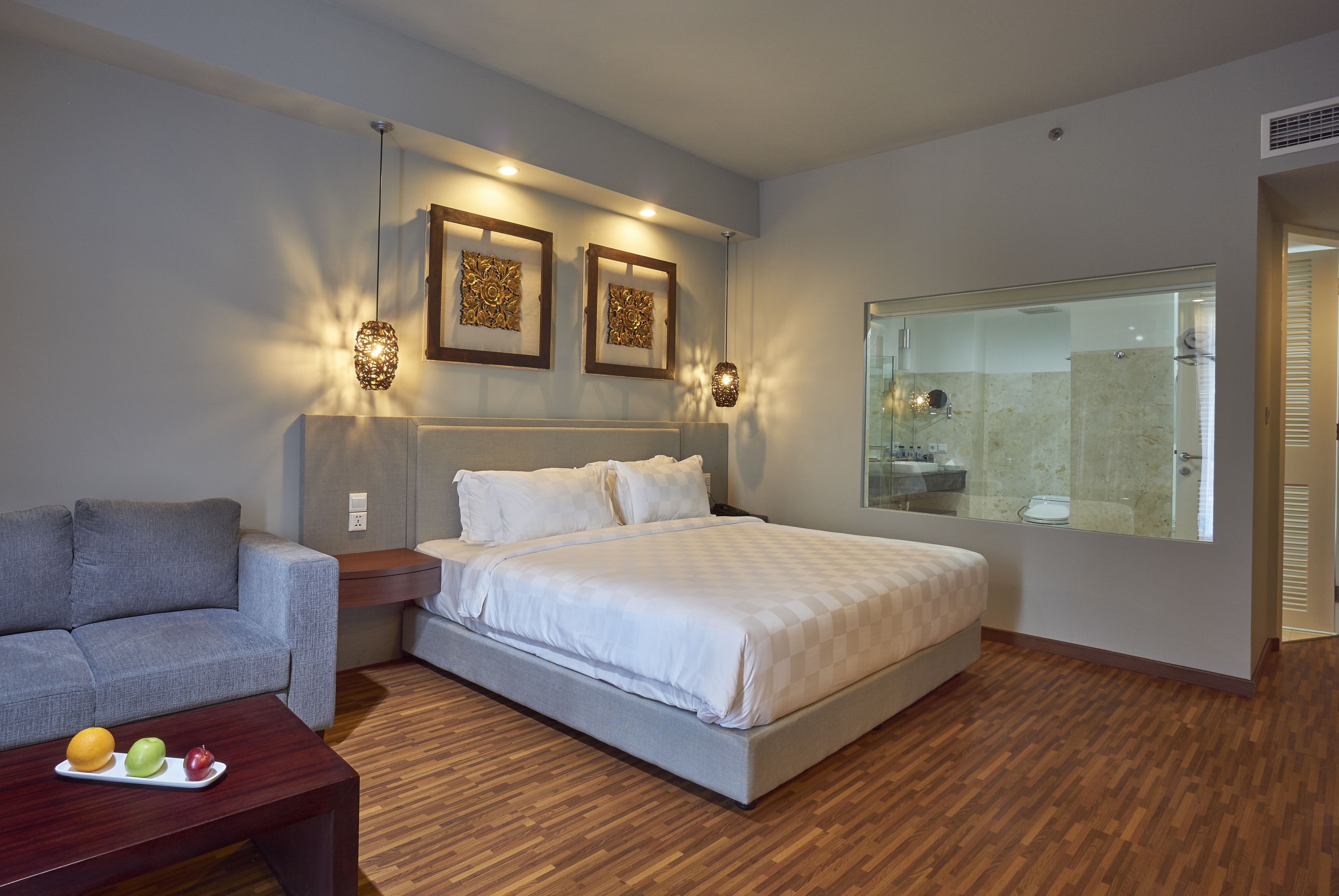 A modern bedroom with a large bed, a gray sofa, a wooden coffee table with fruit, and a large mirror.