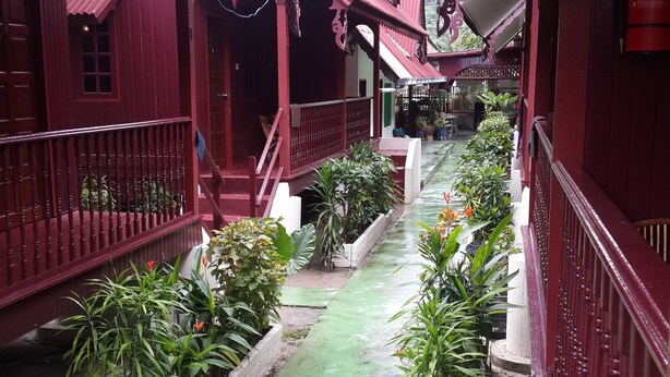 A covered walkway with red railings, potted plants, and a green pathway. - Budget Beach Resort (Pangkor Island)