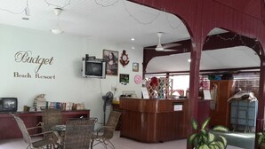 A reception area with wicker furniture, a TV, and a wall with the name 'Budget Beach Resort'. - Budget Beach Resort (Pangkor Island)