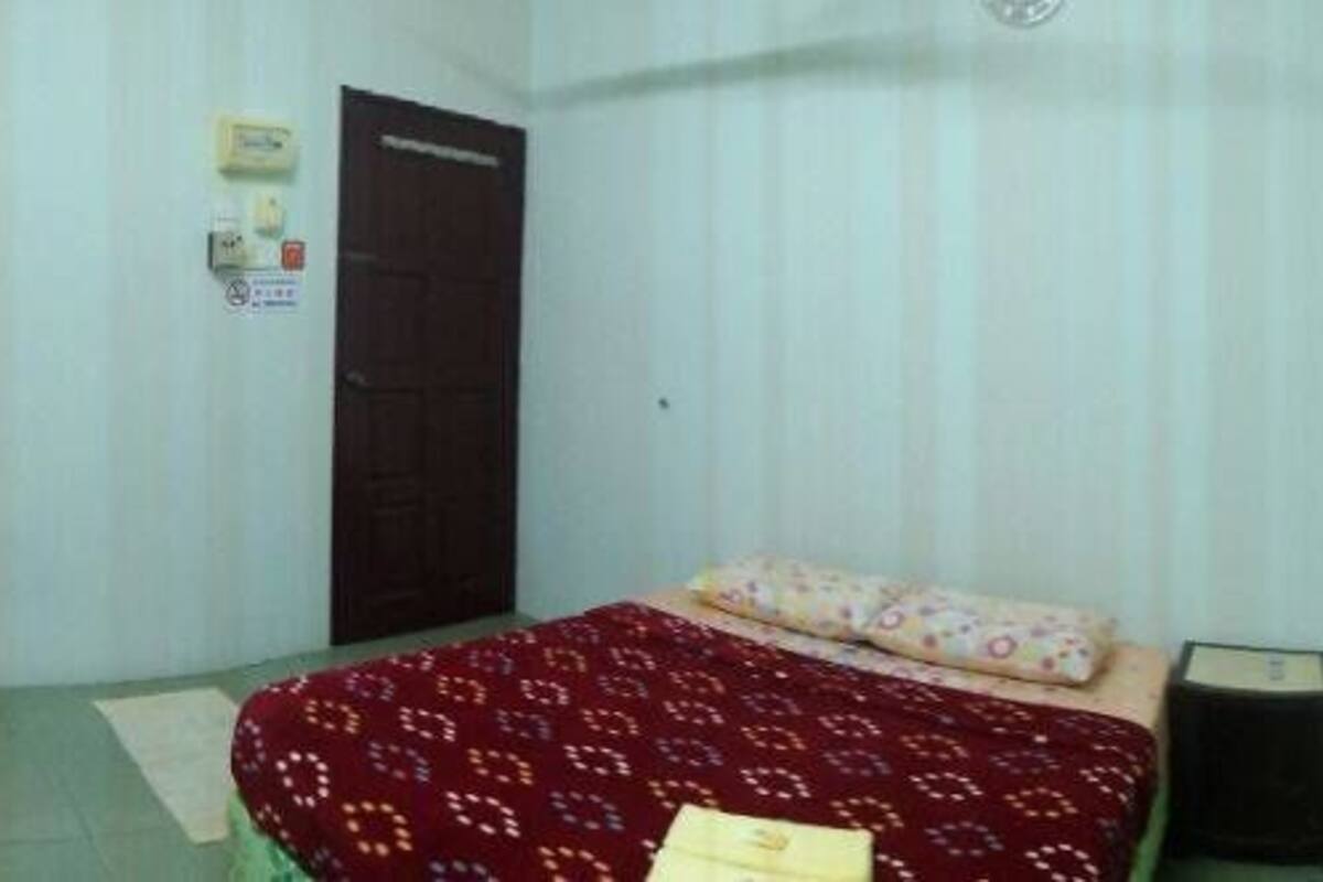 A small, single-bed room with a bed, a bedside table, a shelf, and a door.