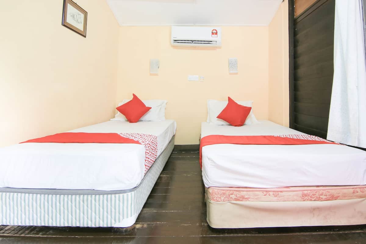 A room with two beds, each with a red pillow and a patterned blanket. There is an air conditioning unit on the wall, and a window with a curtain.