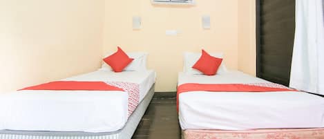 A room with two beds, each with a red pillow and a patterned blanket. There is a ceiling fan and an air conditioning unit above the beds.