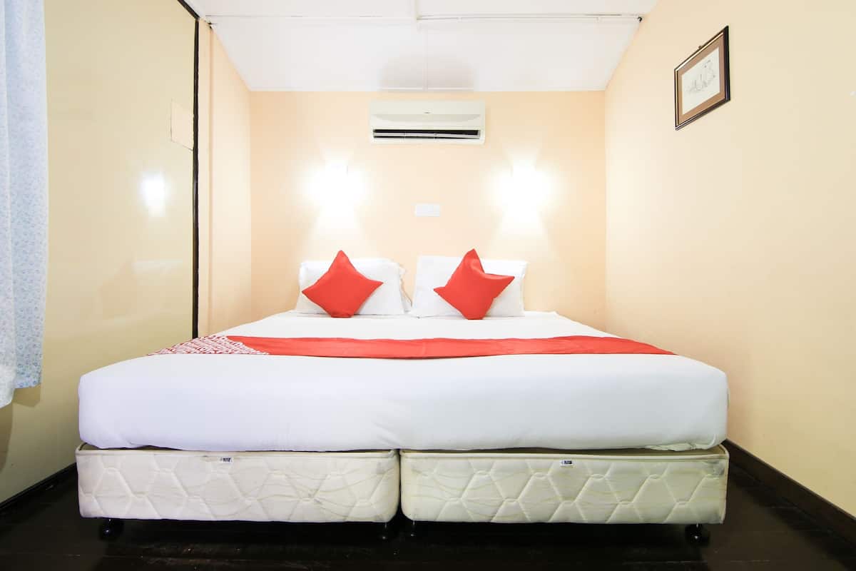 A double bed with white bedding and red pillows, an air conditioning unit on the wall, and a framed picture on the wall.