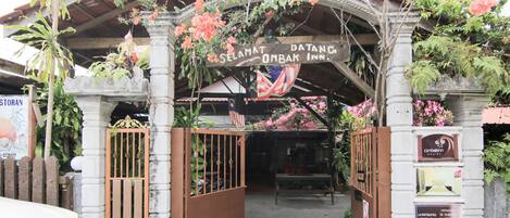The entrance to Selamat Dajang OMBAK Inn, featuring a traditional archway with a sign, a gate, and a bench inside.