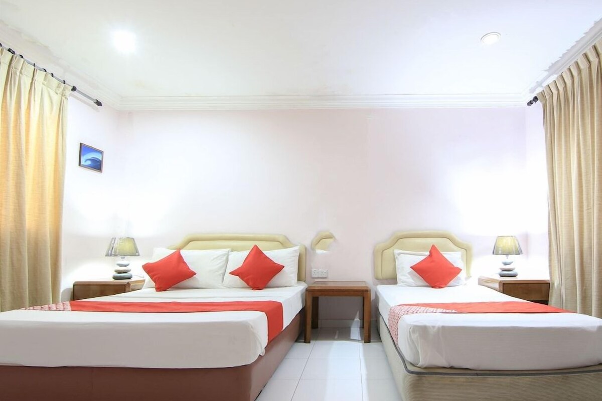 A hotel room with two beds, each with a red pillow, white bedding, and a wooden nightstand with a lamp.