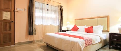 A hotel room with a bed, curtains, a wooden door, and a nightstand with a lamp.