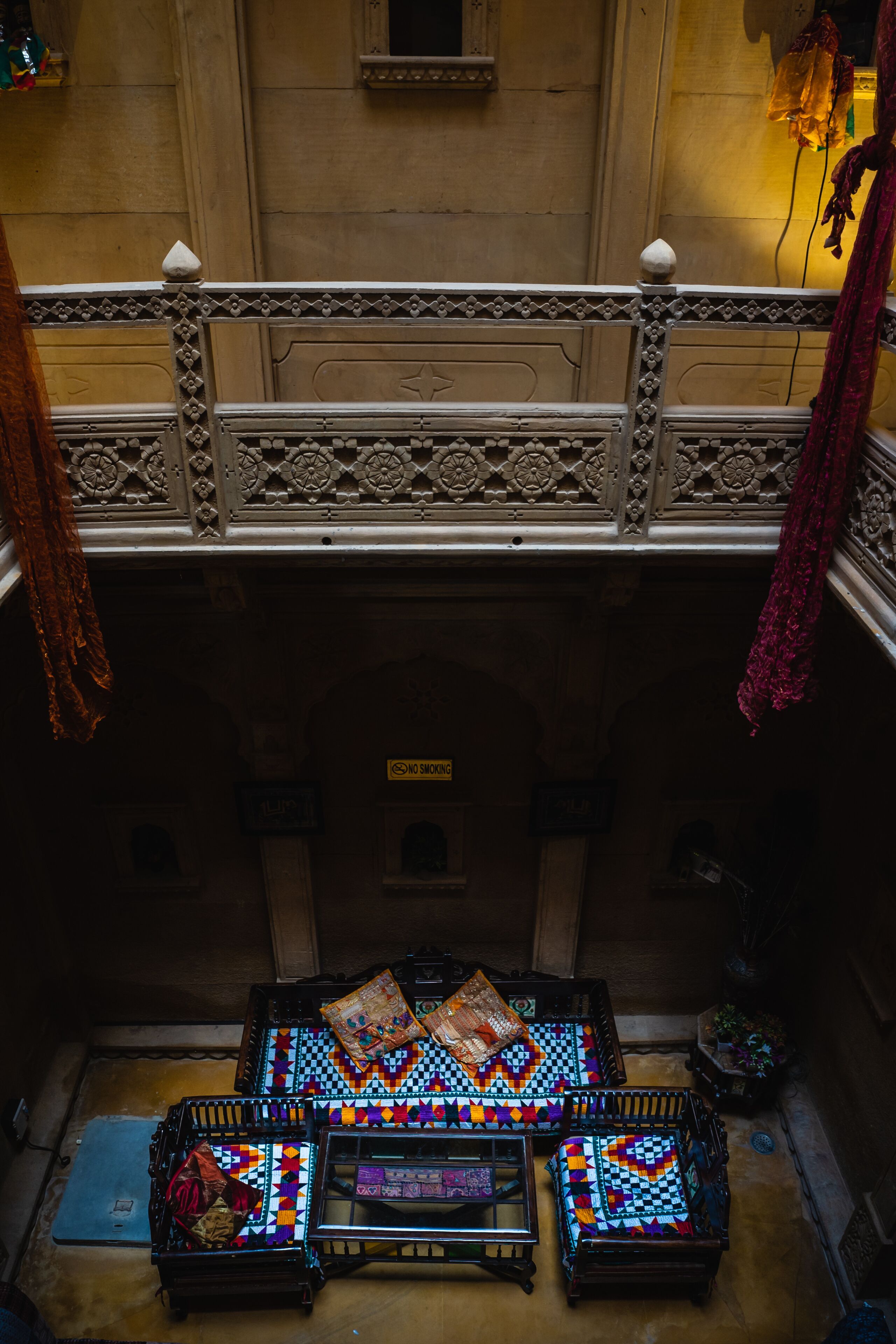 A traditional room with a low ceiling, a balcony with ornate railings, and a checkered floor pattern.