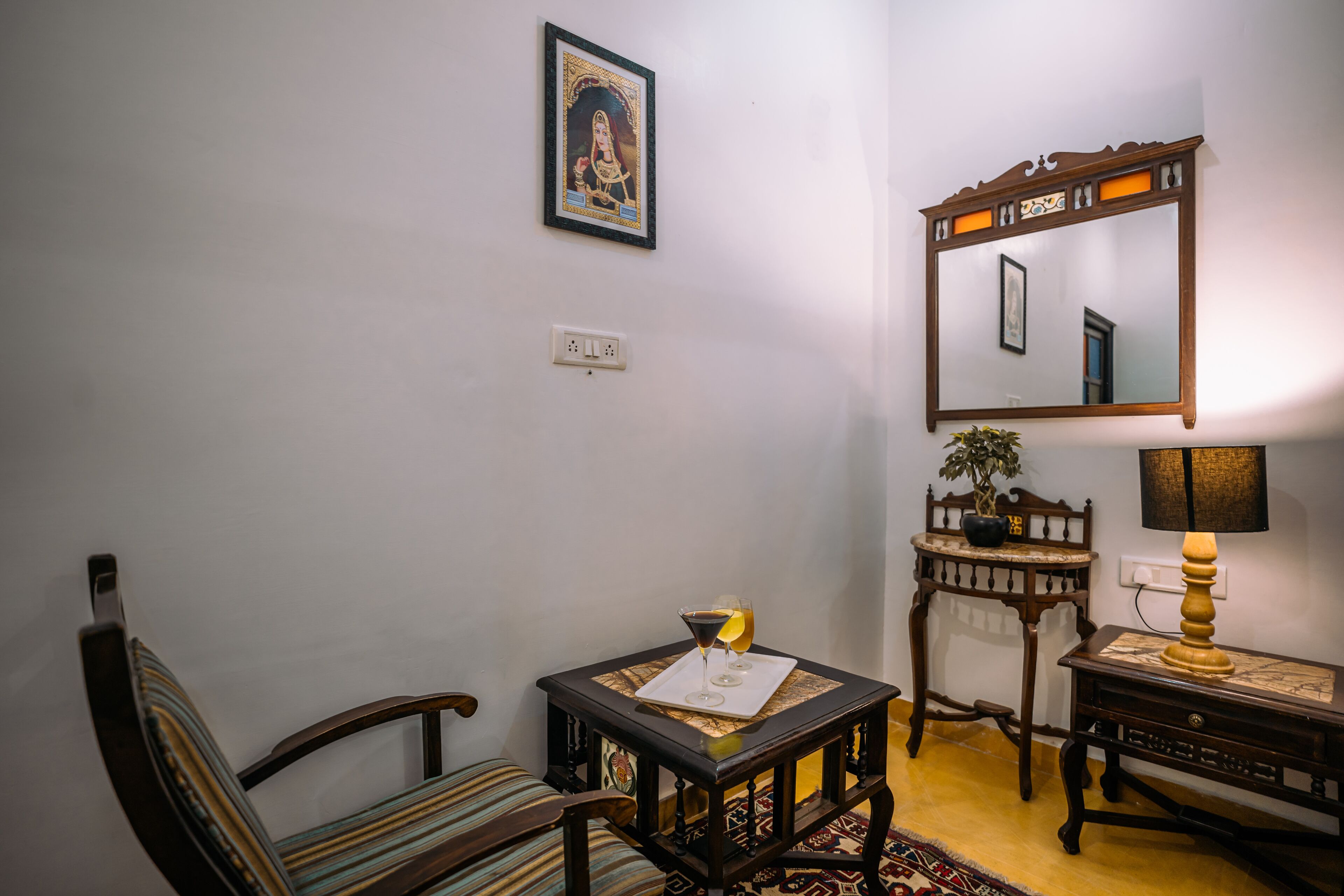 A room with a wooden chair, a small table with a glass and a tray, a mirror, and a lamp.