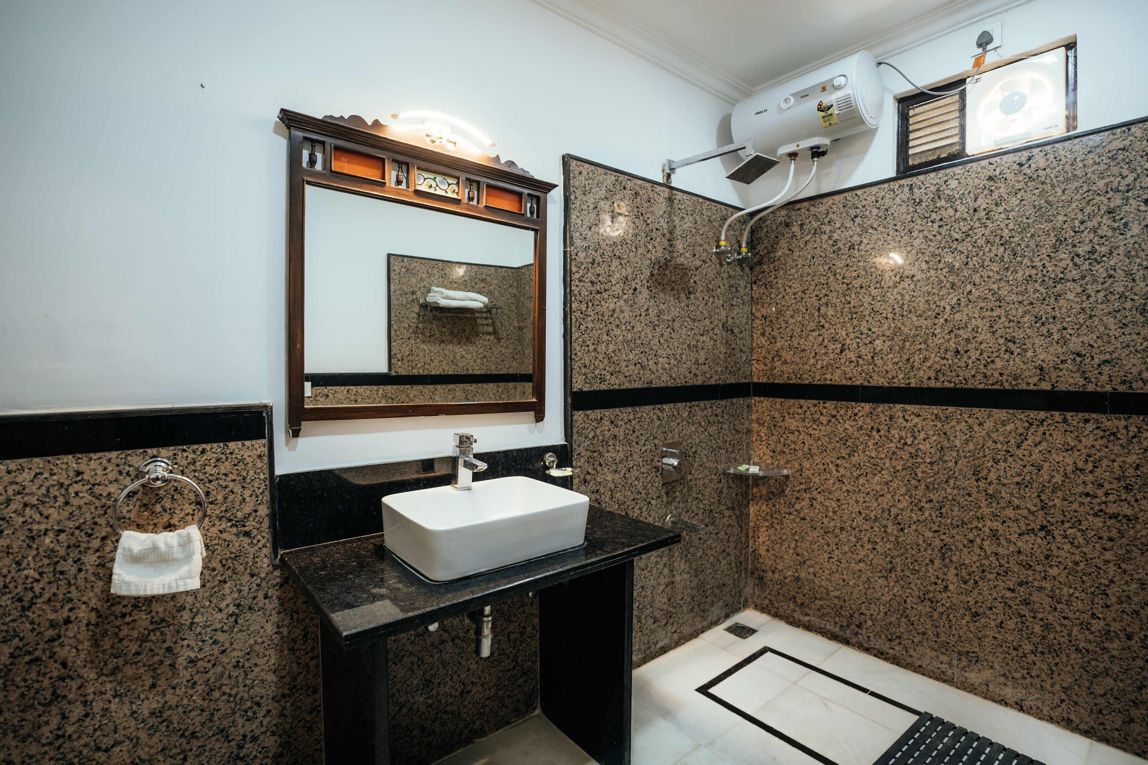 A bathroom with a granite countertop, a white sink, a mirror, and a shower area.