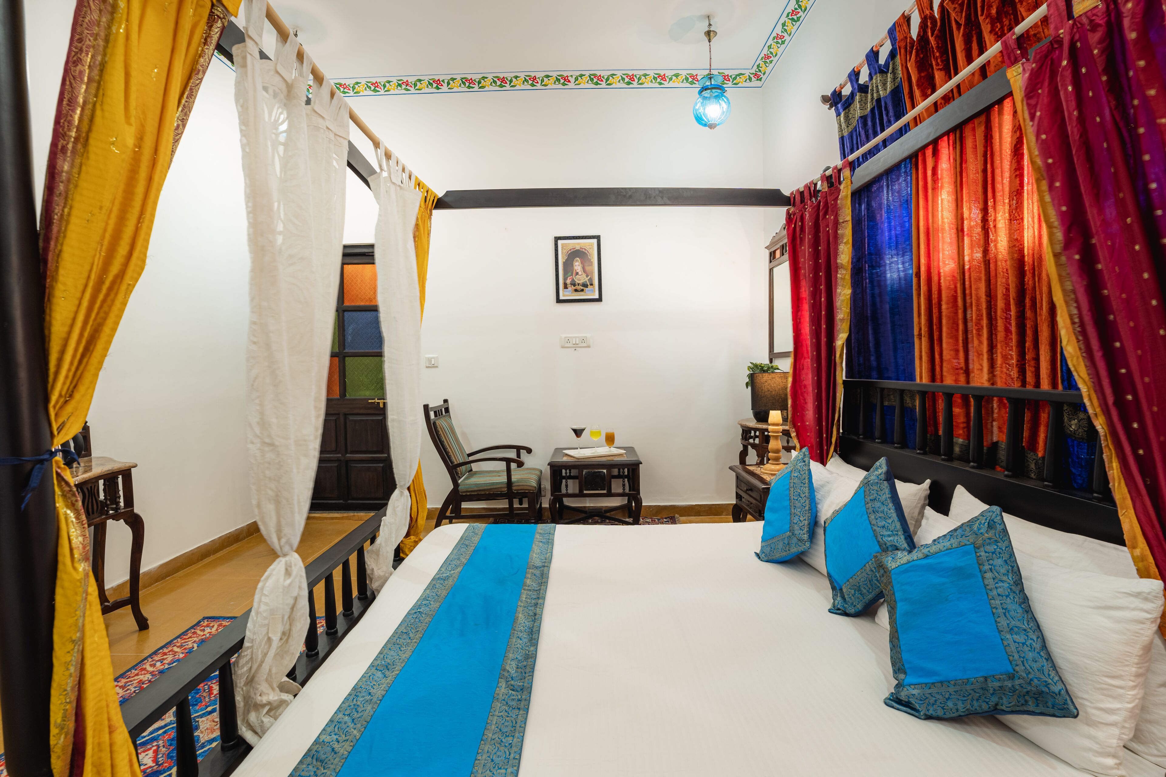 A room with a bed, curtains, a chair, a small table, and a wall-mounted shelf.