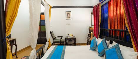 A room with a bed, curtains, a chair, a small table, and a wall-mounted shelf.