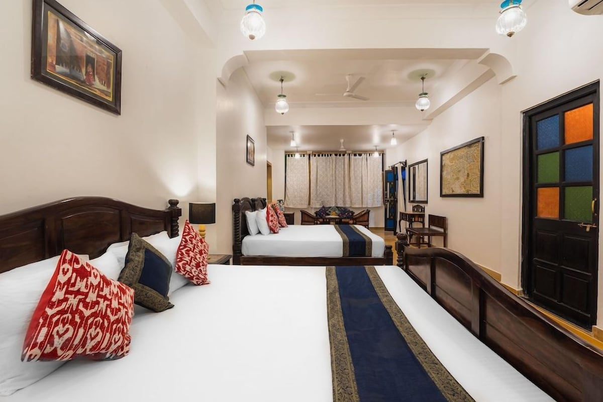 Habitación de hotel con dos camas, un ventanal grande, un ventilador de techo y una puerta con un panel de vidrio colorido.
