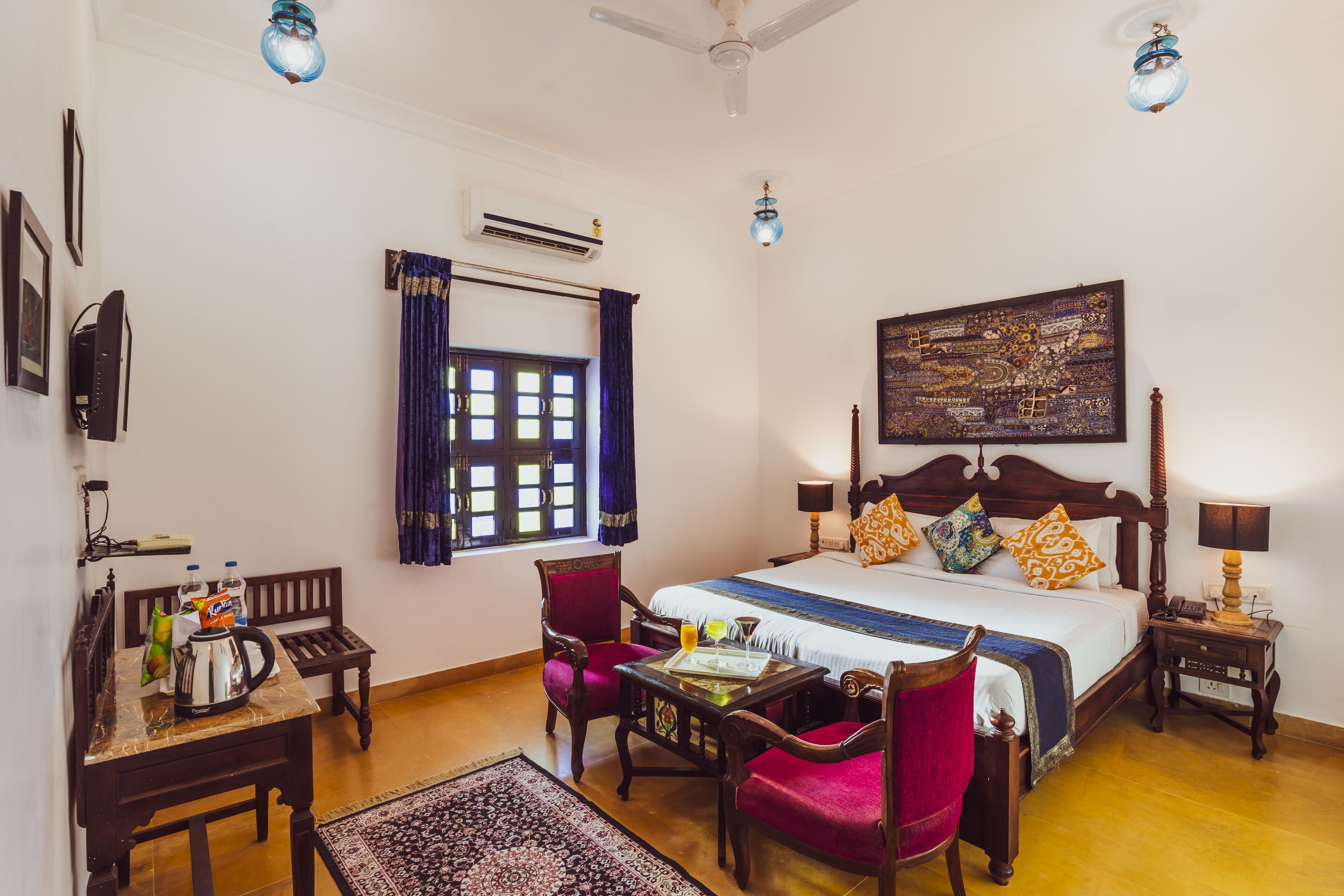 A well-lit room with a bed, a table with a coffee maker, chairs, and a window with curtains.