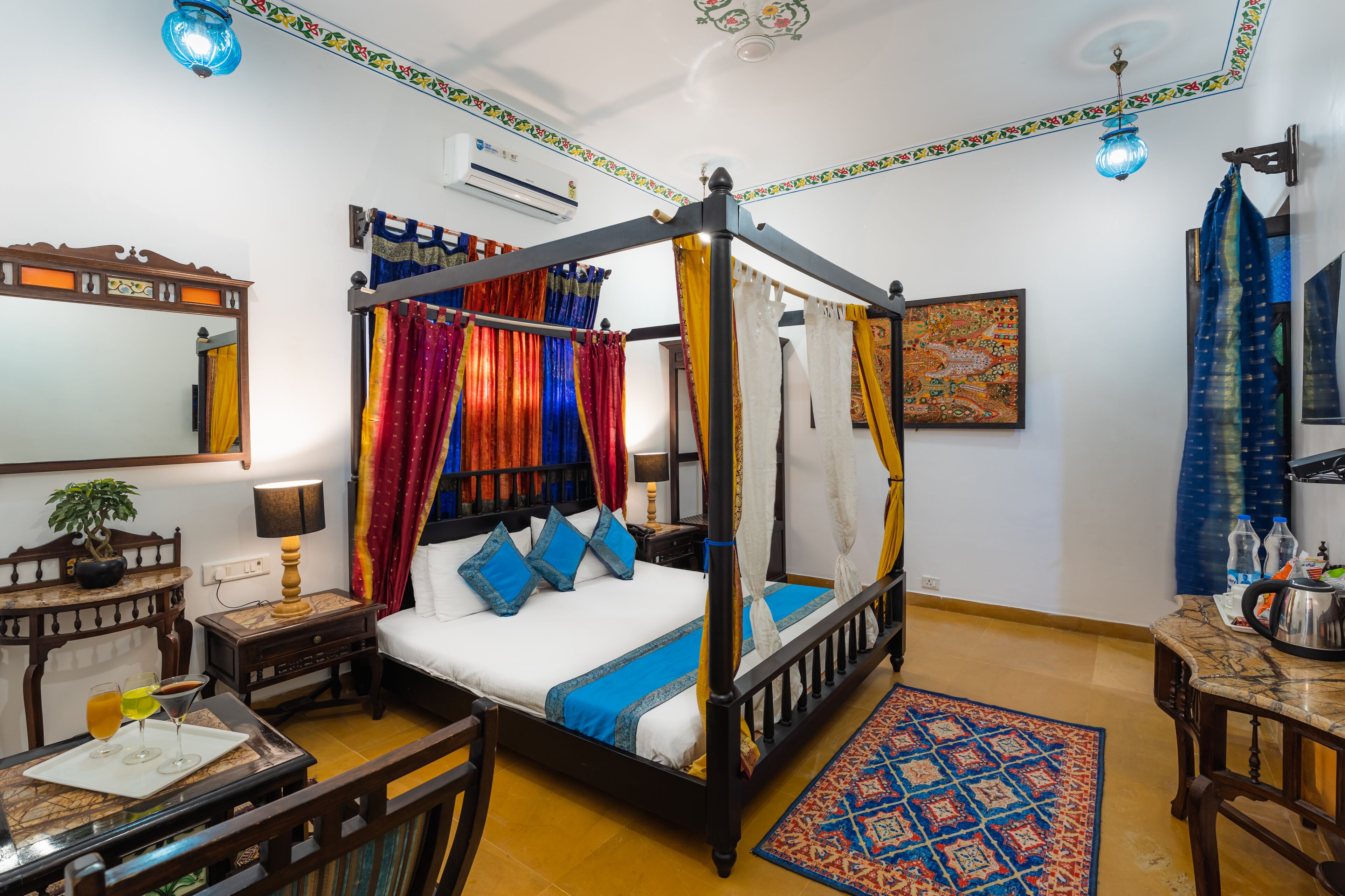 Un lit à baldaquin agrémenté de tentures colorées, une petite table avec des boissons, une table de chevet, un miroir et un plafond décoratif.