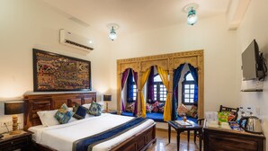 Une chambre spacieuse avec un grand lit, une tête de lit en bois, une décoration murale, un téléviseur et une fenêtre agrémentée de rideaux colorés.