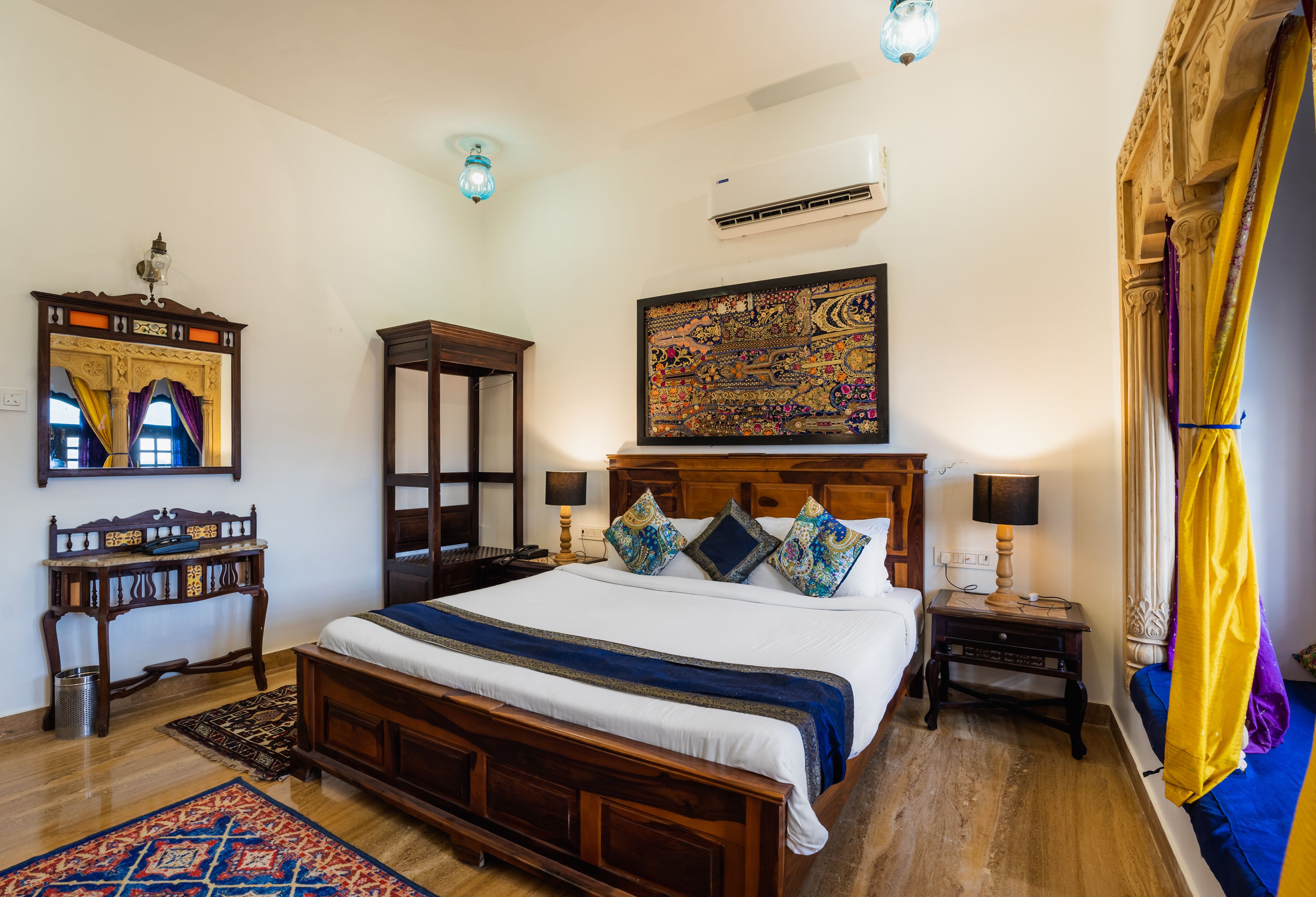 Un dormitorio con una cama grande, una mesita de noche de madera, un escritorio, un espejo y un aire acondicionado de pared.