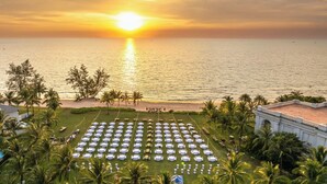 An outdoor seating area with tables and chairs arranged in rows, overlooking a beach and the ocean at sunset.