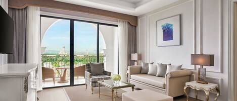A spacious living room with a large sliding glass door leading to a balcony, a sofa set, a coffee table, and a side table with a lamp.
